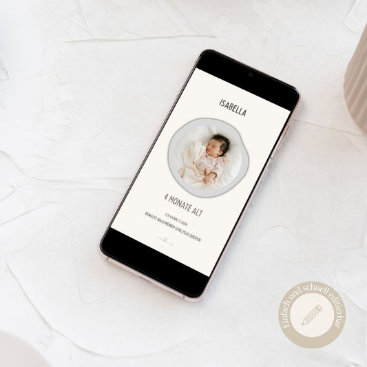 Ein Smartphone liegt auf einer hellen Strukturfläche und zeigt eine personalisierte digitale Baby-Meilensteinkarte in einer Canva-Vorlage für ein 4 Monate altes Baby namens Isabella mit Foto.